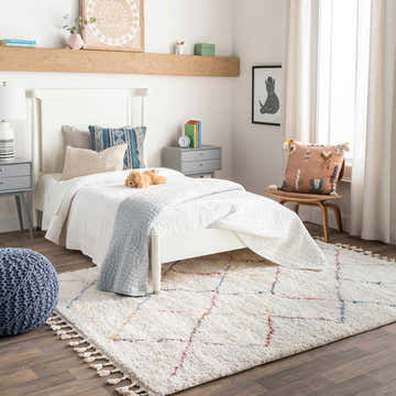 Bedroom scene with a white bed, gray nightstands, and the Tigao Area Rug in cream with colorful accents. Roomscene-Rectangle