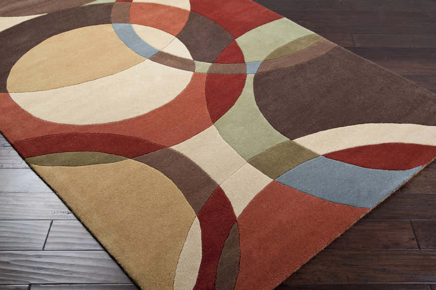 Close-up of the Tilbury Modern Hand Tufted Wool Rug featuring a geometric pattern in brick red, brown, tan, and blue hues. Corner