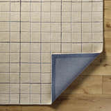 Close-up of the Toshi Beige Area Rug. Hand-tufted wool rug with a contemporary grid pattern in beige, black, and gray. Fold