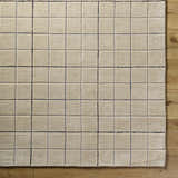 Close-up of the Toshi Beige Area Rug. Hand-tufted wool rug with a contemporary square grid pattern in tan, gray, and black. Corner