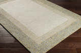 Close-up of the hand-tufted Tandayag Area Rug. Cream center with light beige and dusty sage striped border on dark wood floors. Corner
