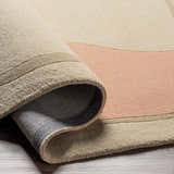 Close-up of the hand-tufted Tomingad Area Rug showing its oatmeal, dusty pink, and taupe geometric design and wool texture. Fold