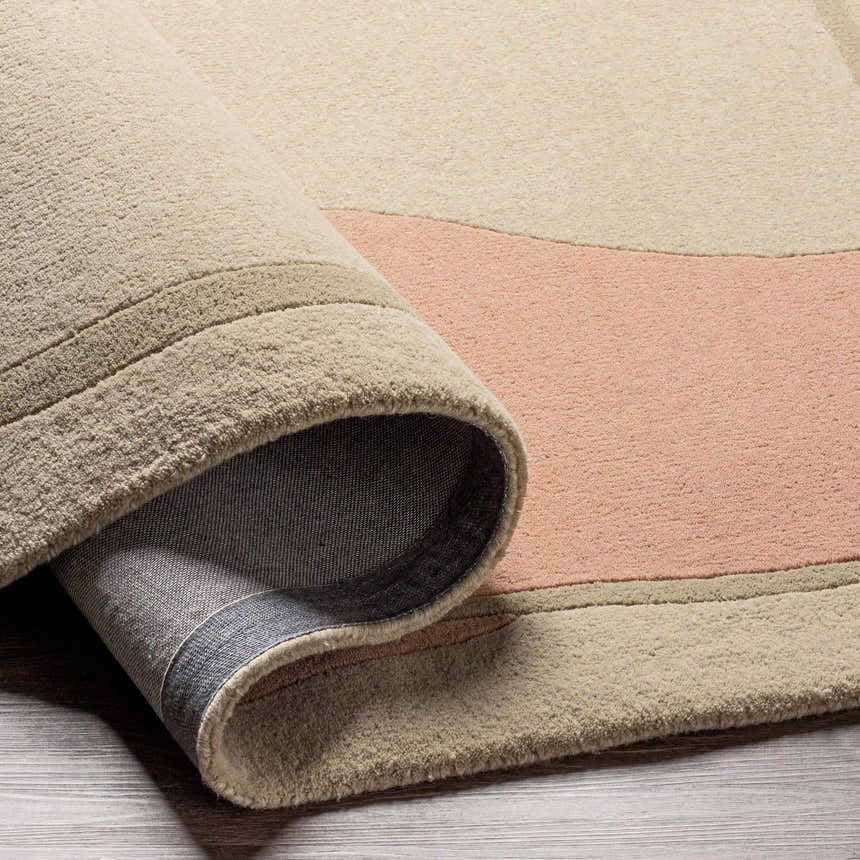 Close-up of the hand-tufted Tomingad Area Rug showing its oatmeal, dusty pink, and taupe geometric design and wool texture. Fold