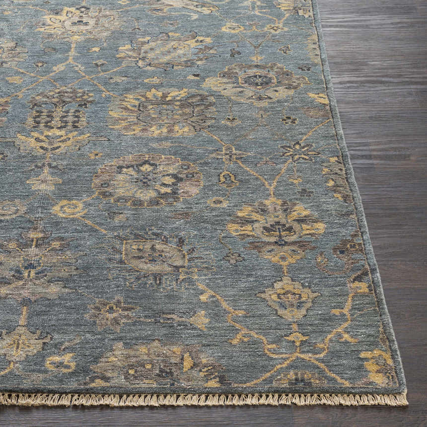 Close-up of the hand-knotted Toquerville Premium Rug. Aqua rug with charcoal, oatmeal, and wheat floral pattern on dark wood floor. Front