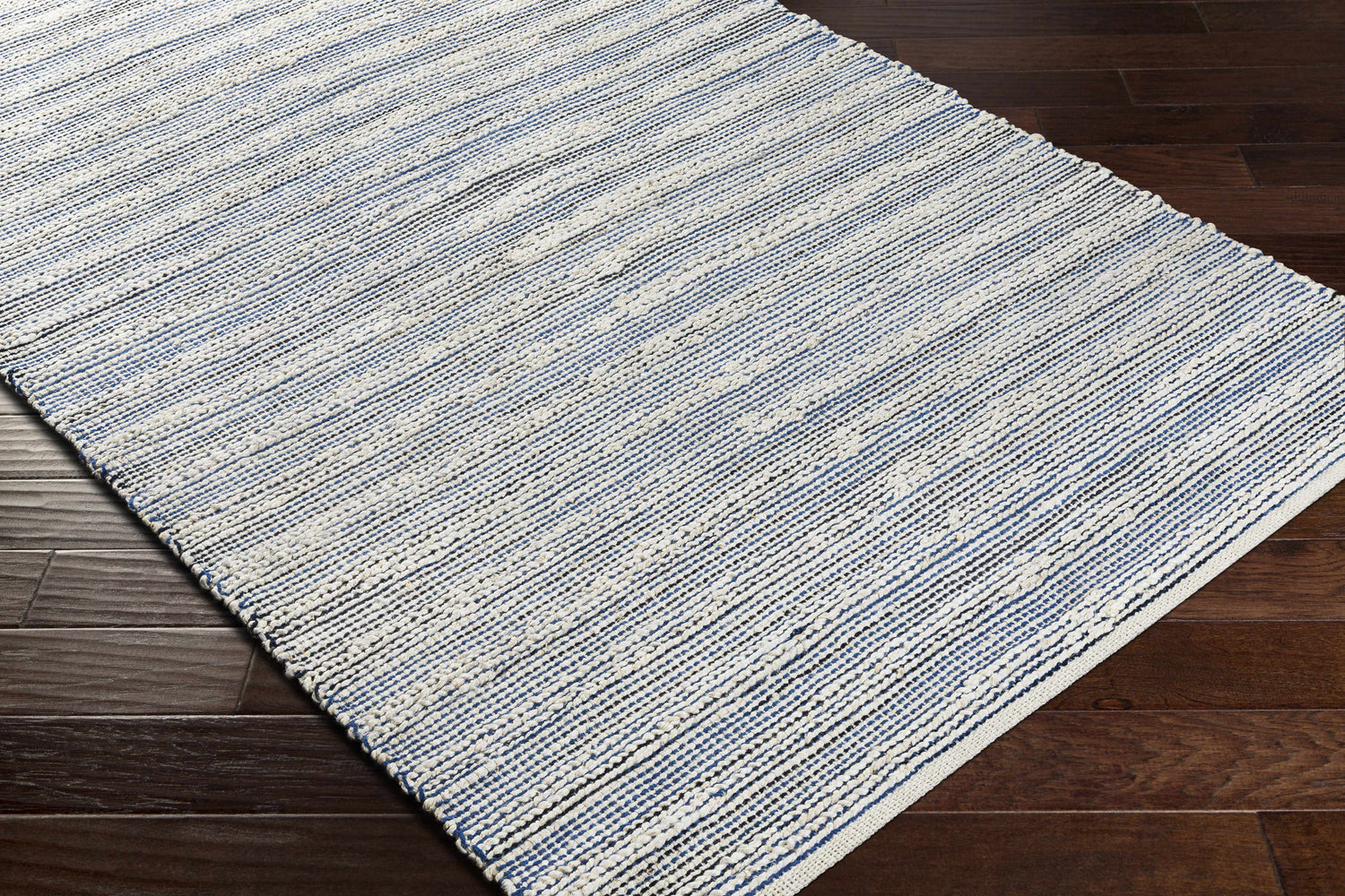 Close-up of the hand-woven Totolan Area Rug. Beige, denim, and black jute stripes on dark wood floor. Coastal Grandmother style. Corner