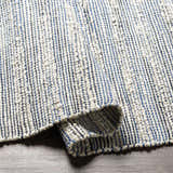 Close-up of the hand-woven Totolan Area Rug. Beige jute rug with a denim blue striped pattern and textured weave. Fold