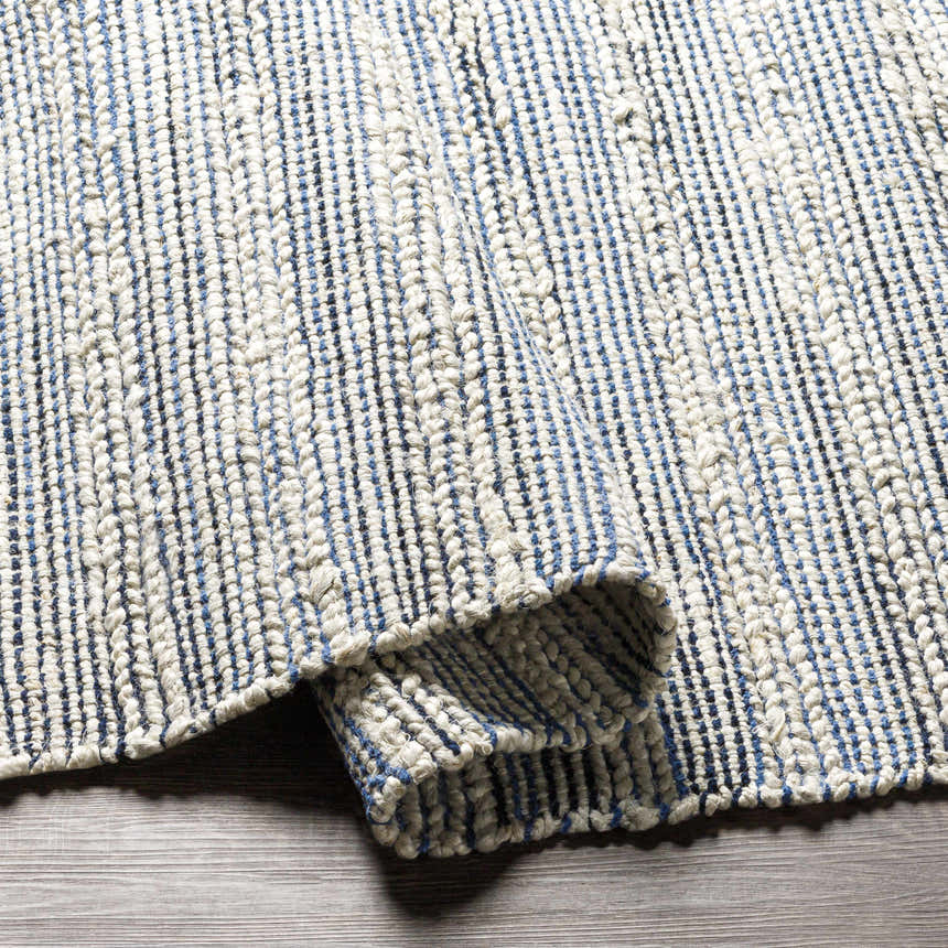 Close-up of the hand-woven Totolan Area Rug. Beige jute rug with a denim blue striped pattern and textured weave. Fold