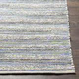 Close-up of Totolan area rug showing beige jute with denim and black stripes. Hand-woven texture detail. Front