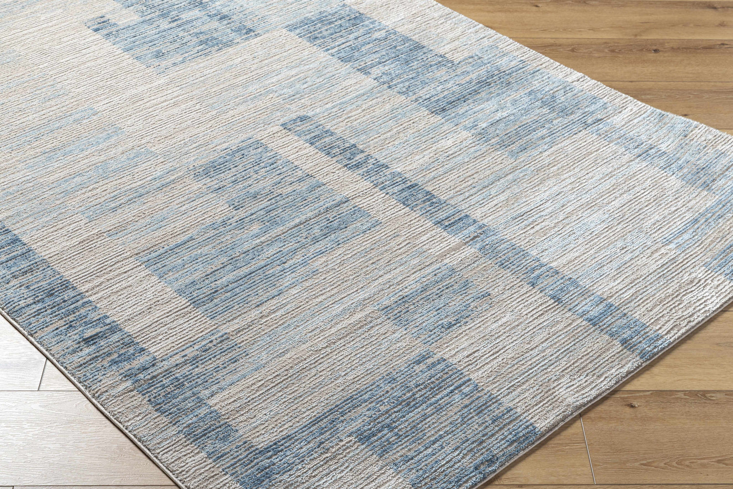 Close-up of the Teman Area Rug, a contemporary design in blue and ivory, machine woven with a subtle geometric pattern. Corner