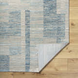 Close-up of the Teman Area Rug showing its blue, ivory, and tan contemporary pattern and machine-woven texture. Fold