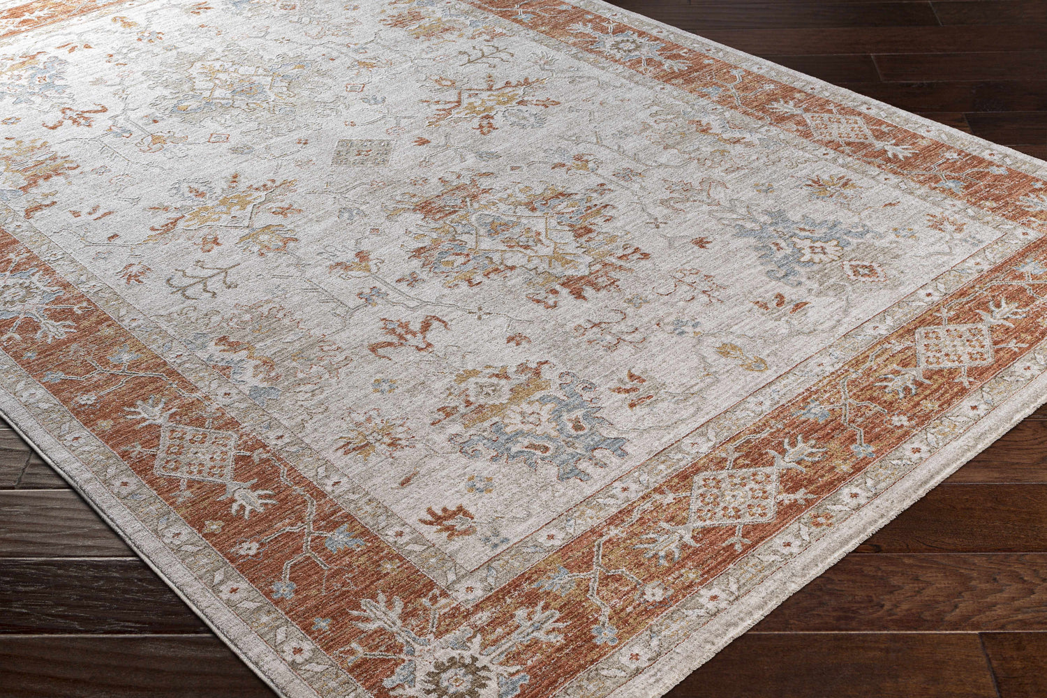 Close-up of Tsawwassen Thick Luxe Area Rug. Features brick red, light beige, and blue traditional patterns. Machine woven texture. Corner