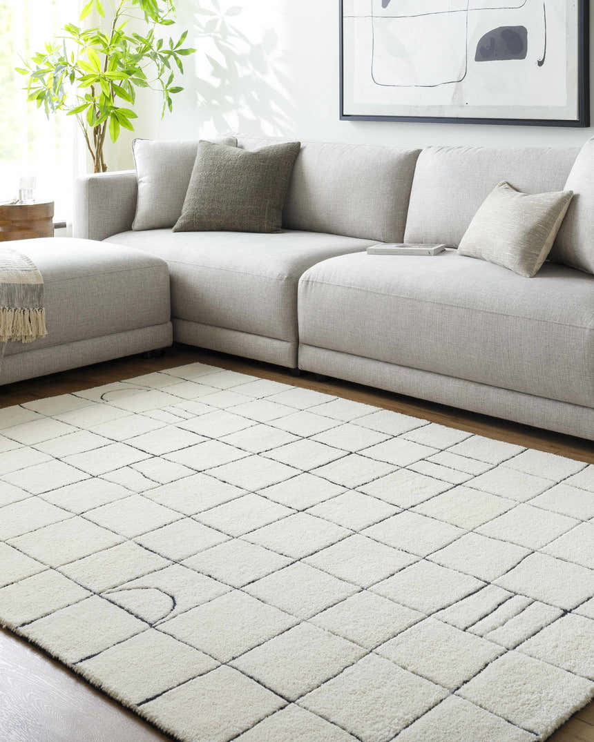 Living room scene with a light gray sectional sofa and the Tuuka Pearl Area Rug with a geometric grid pattern. Roomscene-Rectangle