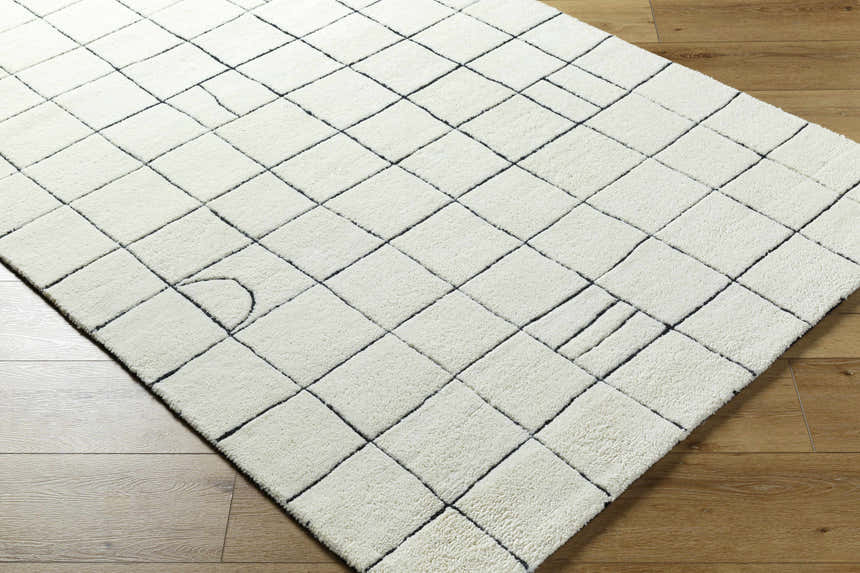 Close-up of the Tuuka Pearl Area Rug. Hand-tufted cotton and wool rug with a geometric grid pattern in pearl white and black. Corner