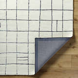 Close-up of Tuuka Pearl Area Rug showing its pearl color, grid pattern, hand-tufted texture, and the rug's backing. Fold