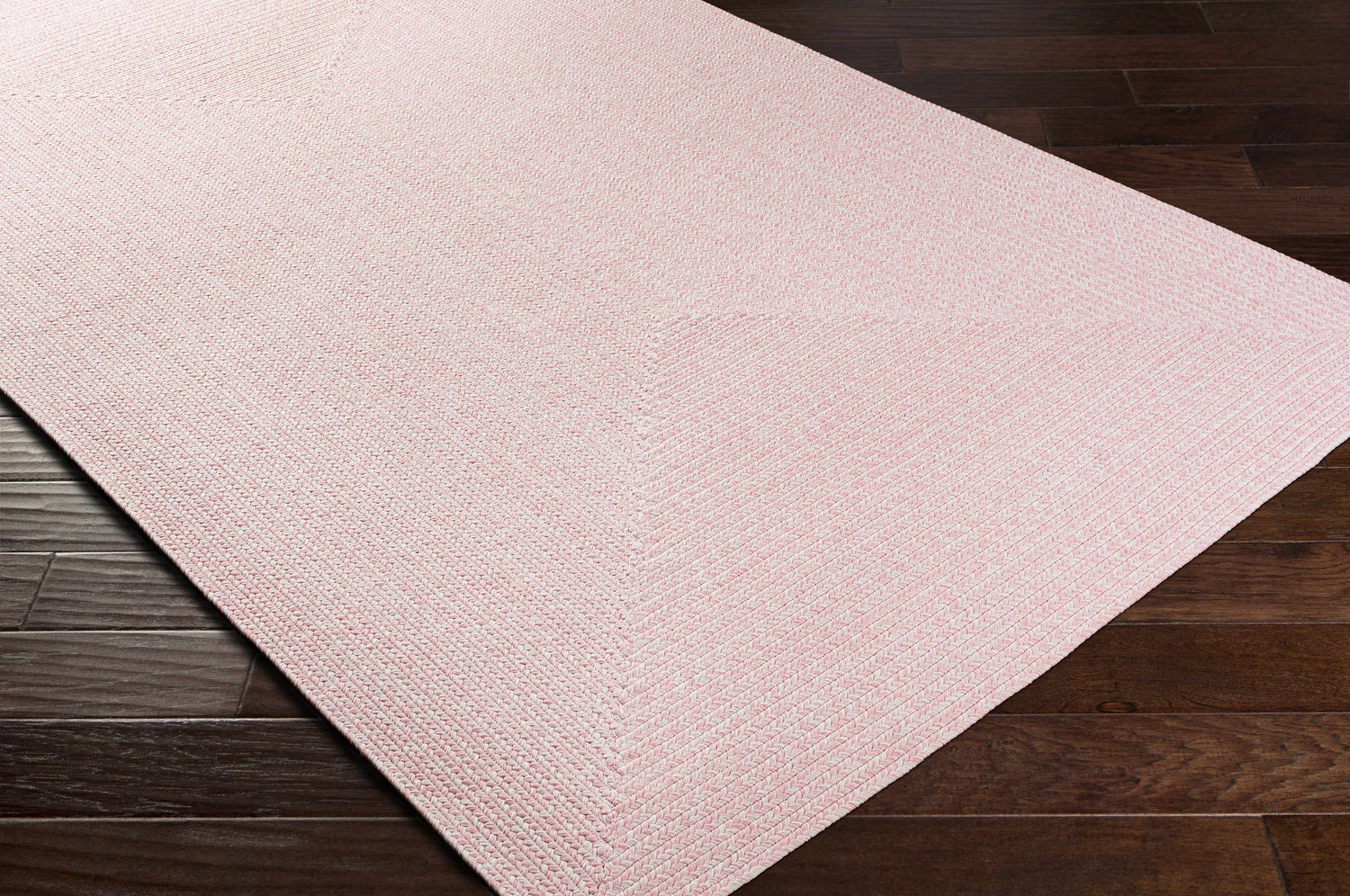 Close-up of the Pink Tycroes Braided Textured Area Rug showing its weave and color on a dark wood floor. Corner