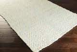 Close-up of the Tyronza Clearance Jute Rug. Hand-woven rug features a cream and sky blue diamond pattern and natural texture. Corner