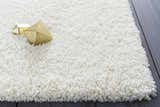 Close-up of the cream Umpire Area Rug, a hand-woven shag rug with geometric gold accents on a dark wood floor. Styleshot