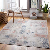 Coastal living room scene with the Upminster Area Rug in brick red, charcoal, and beige. Wicker chair and wood accents. Roomscene-Rectangle