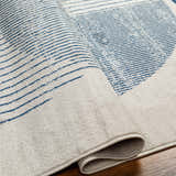 Close up of the Usra Area Rug featuring a geometric pattern with harbor blue stripes on a natural gray background. Fold