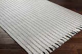Close up of the Varennes Area Rug, a cream wool rug with thin black stripes and fringe, on dark wood floors. Corner