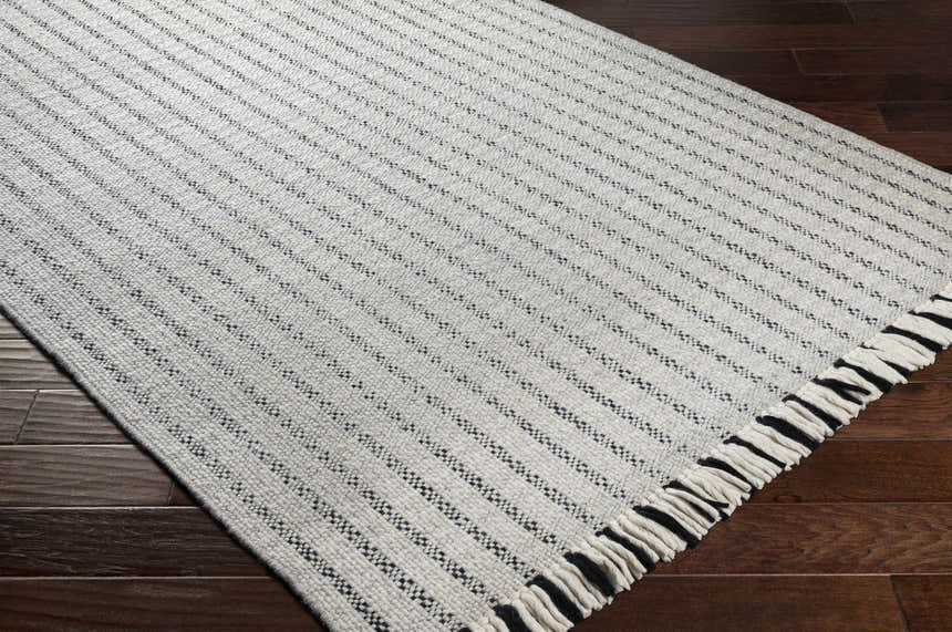 Close up of the Varennes Area Rug, a cream wool rug with thin black stripes and fringe, on dark wood floors. Corner