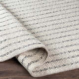 Close-up of the Varennes Area Rug. Cream wool rug with thin black stripes, hand woven texture. Fold