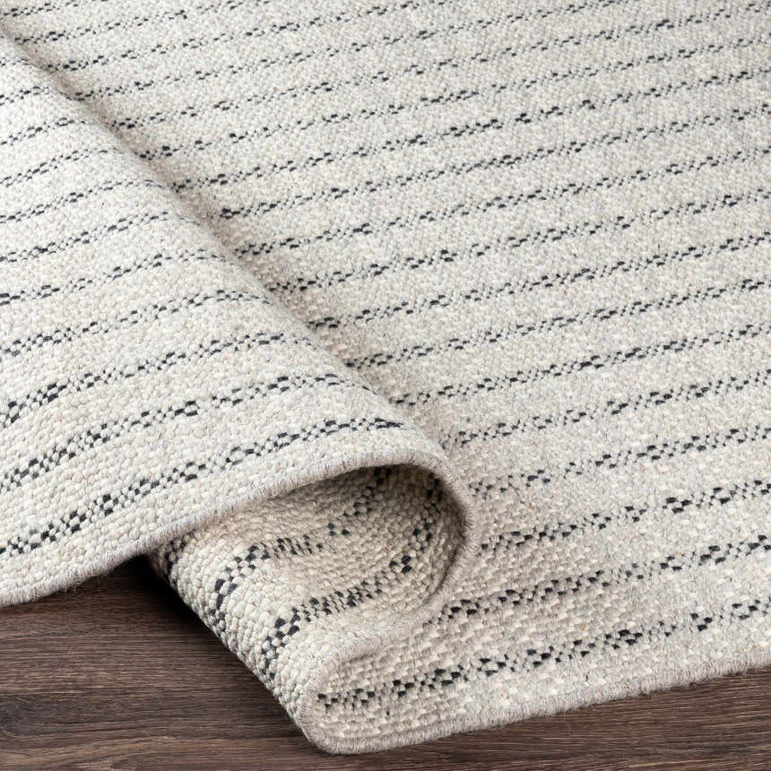 Close-up of the Varennes Area Rug. Cream wool rug with thin black stripes, hand woven texture. Fold