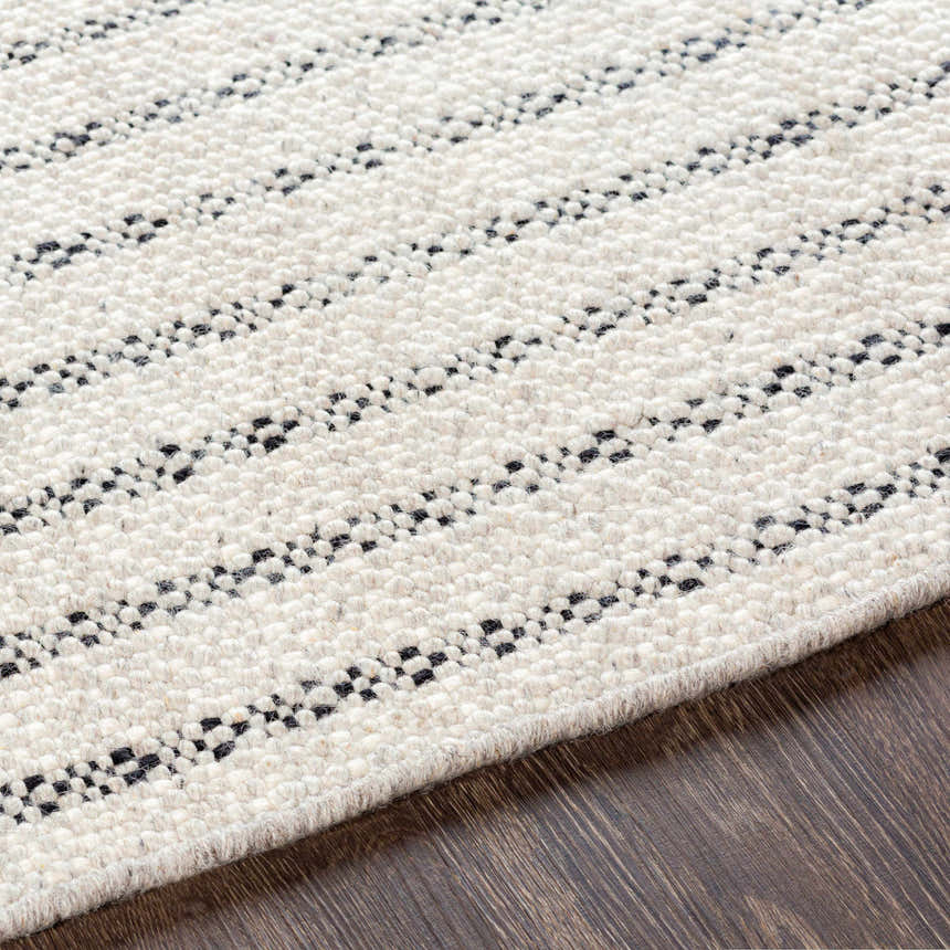 Close-up of the hand woven Varennes Area Rug. Cream wool rug with a black striped pattern and textured detail. Texture