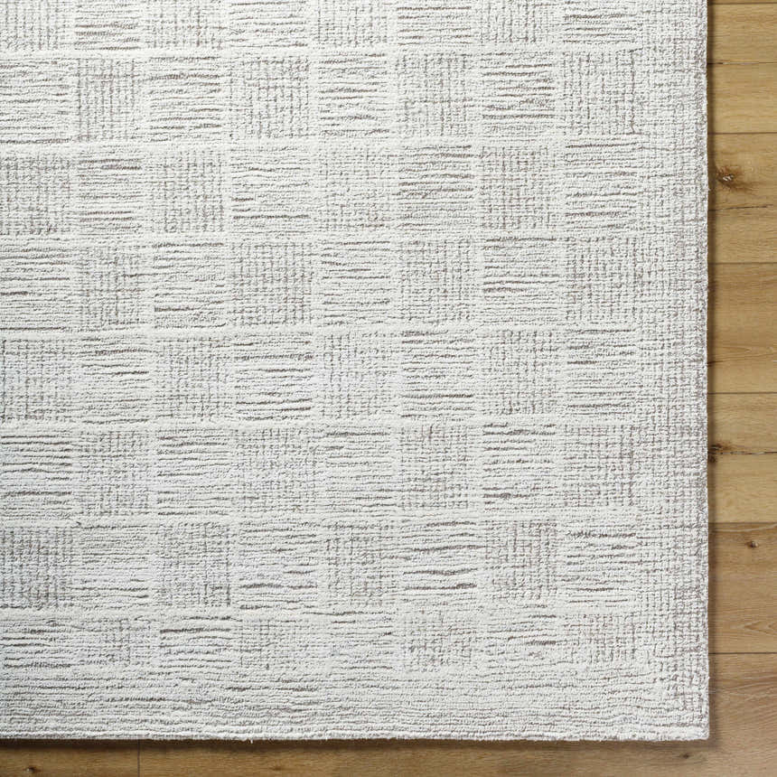 Close up of the hand tufted Urian Area Rug in light silver and silver gray on wood flooring. Corner
