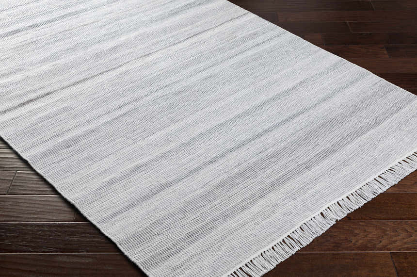 Close-up of the hand-woven Villasis Area Rug in gray, light beige, and off-white on a dark wood floor. Corner
