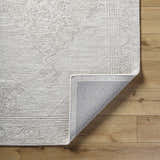 Close-up of the ash-colored Verne Area Rug showing its hand-tufted wool texture and traditional pattern on wood flooring. Fold