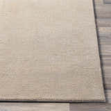 Close-up of the tan, hand-loomed texture of the Brockton Solid Wool Area Rug on wood flooring. Front
