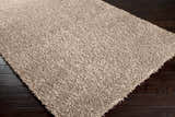 Close-up of the Browder Solid Beige Shag Area Rug showing its plush texture and color against dark wood floors. Corner