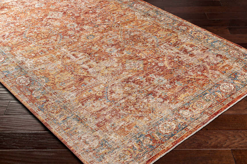 Close-up of the Wetaskiwin Area Rug. Bohemian style with brick red, burnt orange, and blue tones on dark wood floors. Corner