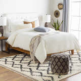Bedroom scene with a Bohemian style Ogallah Area Rug, white bedding, and a patterned ottoman. Styleshot