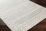 Close-up of the Winston Area Rug, a cream and gray rug with a geometric bohemian pattern on dark wood flooring. Corner