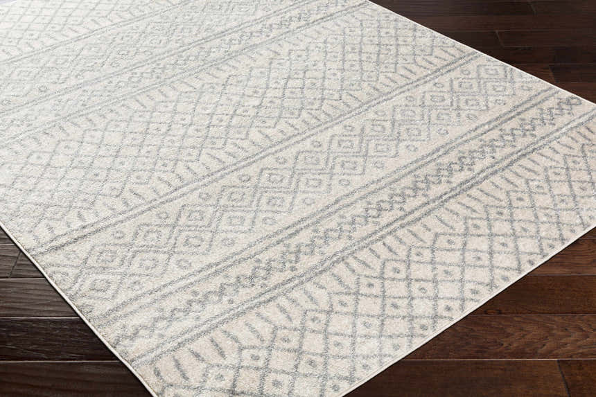 Close-up of the Winston Area Rug, a cream and gray rug with a geometric bohemian pattern on dark wood flooring. Corner