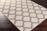 Close-up of the Winterville Area Rug, showcasing its beige and dark red quatrefoil pattern on a dark wood floor. Corner