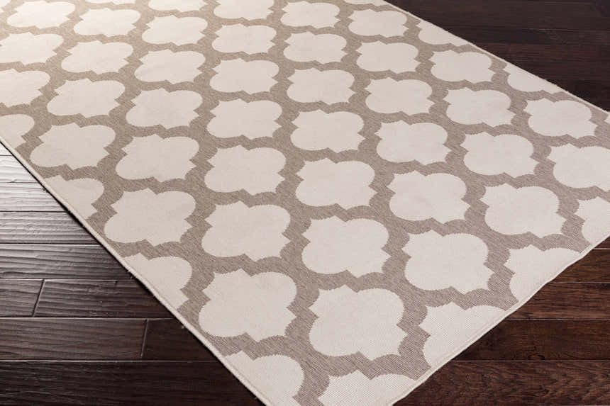 Close-up of the Winterville Area Rug, showcasing its beige and dark red quatrefoil pattern on a dark wood floor. Corner