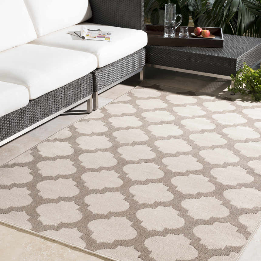 Patio scene with a beige Winterville Area Rug featuring a quatrefoil pattern, white sofa, and dark wicker table. Roomscene-Rectangle