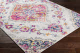 Wallsburg Magenta & Cream Area Rug detail. Bohemian floral pattern in magenta, saffron, navy, and cream on dark wood floor. Corner
