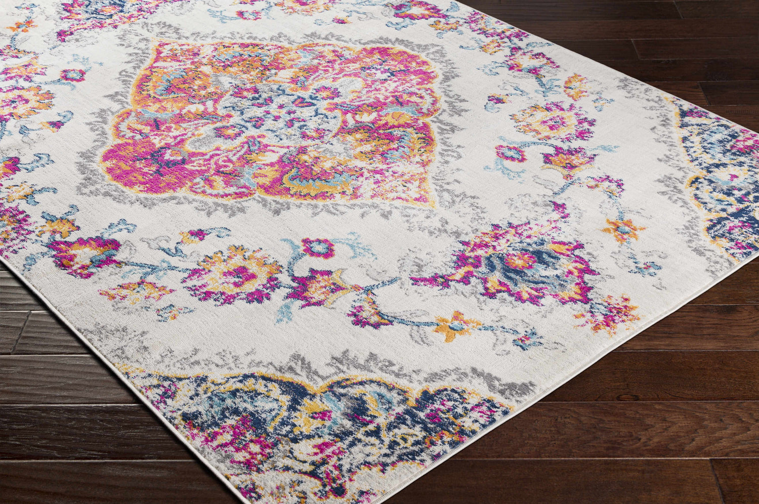 Wallsburg Magenta & Cream Area Rug detail. Bohemian floral pattern in magenta, saffron, navy, and cream on dark wood floor. Corner