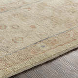 Close-up of the hand-knotted Wooroloo Area Rug. Beige wool rug with dusty pink, gray, and tan accents. Traditional design. Texture