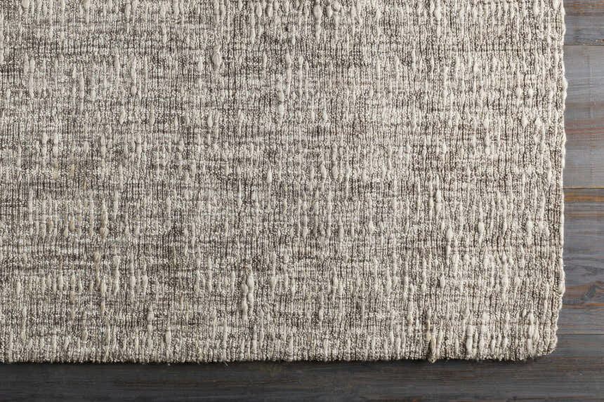 Close-up of the hand-loomed Westoning Area Rug. Neutral colors, textured weave, and rectangular shape on dark wood floor. Corner