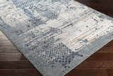 Close-up of the Waterboro Area Rug, a contemporary rug in shades of gray, blue, ivory, and black on a dark wood floor. Corner