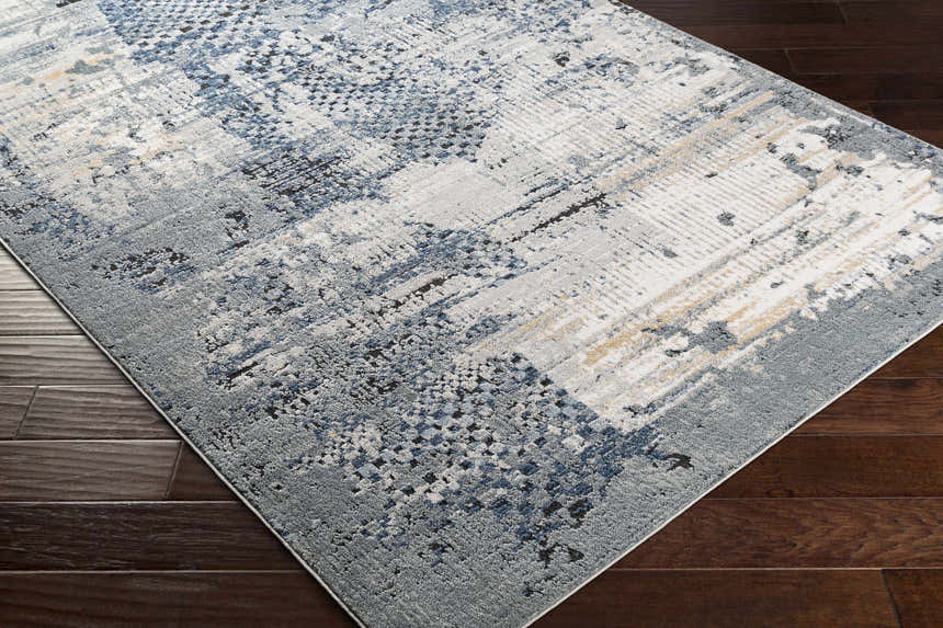 Close-up of the Waterboro Area Rug, a contemporary rug in shades of gray, blue, ivory, and black on a dark wood floor. Corner