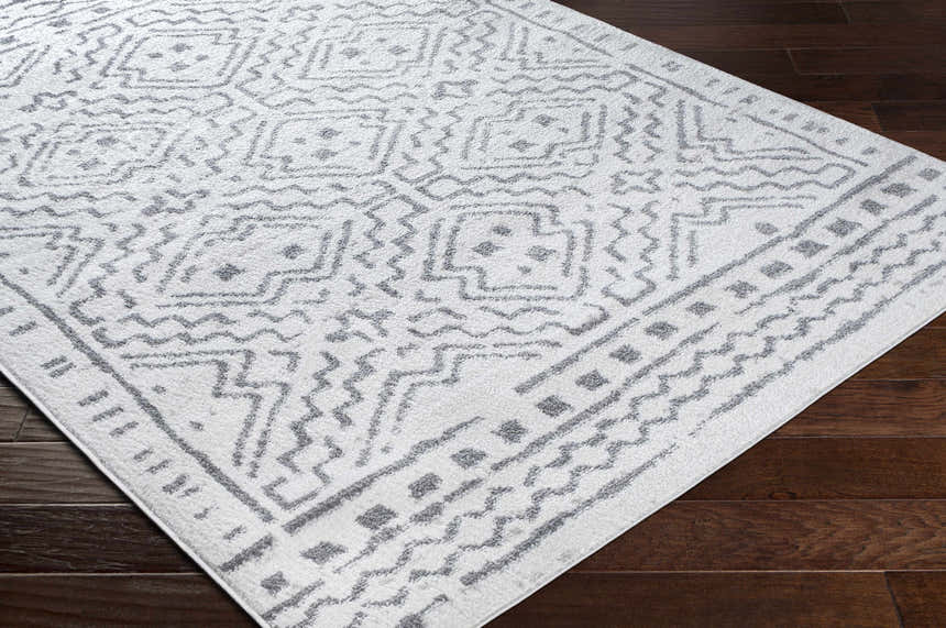 Close-up of the Watertown Area Rug, a machine-woven rug in gray and white with a geometric pattern on dark wood floors. Corner