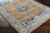 Close-up of the Trotters Orange/Blue Performance Rug showing its bohemian-inspired design and rich brick red, brown, and navy colors. Corner