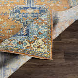 Close-up of the Trotters Orange/Blue Performance Rug showing its bohemian-inspired design, colors, and texture on a wood floor. Fold