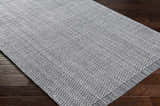 Close-up of a hand loomed light gray area rug with a subtle textured pattern on dark wood floors. Clearance rug. Corner